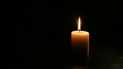 Single candle lit and glowing on a black background.